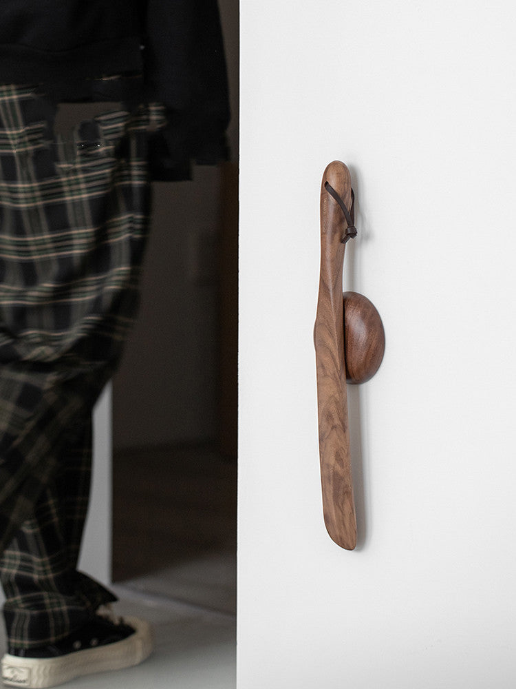 Walnut shoe horn hanging on its magnetic wall disc beside the door